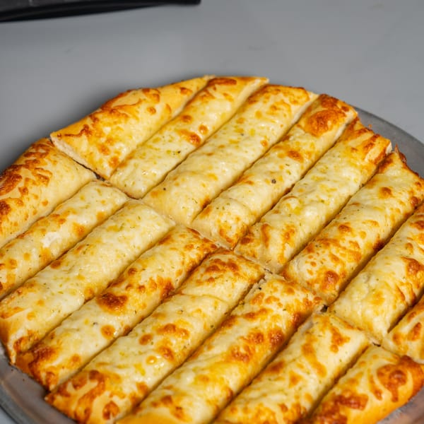 Ruszoni's Pizza's cheesy breadsticks, golden brown and cut into strips, on a metal pizza pan.