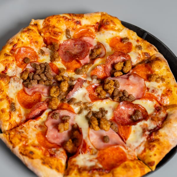 Ruszoni's Pizza with pepperoni, ham, and sausage, on a dark pan against a light background.