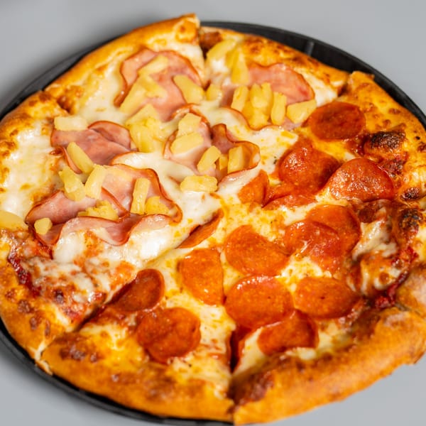 Half pepperoni and half ham and pineapple pizza on a black pan.