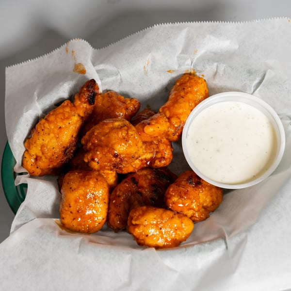 A basket of Ruszoni's Pizza boneless wings coated in orange sauce, with a side of ranch.