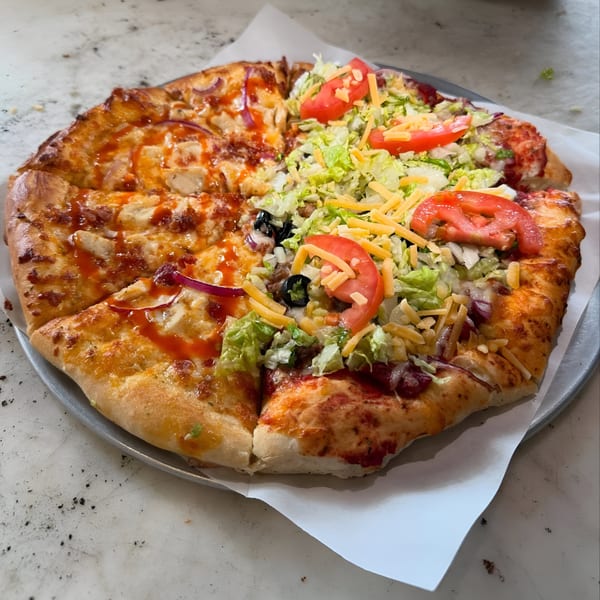 A Ruszoni's Pizza with half BBQ chicken and half taco pizza with lettuce, tomatoes, and cheese.