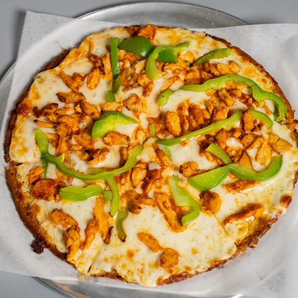 Ruszoni's Pizza with melted cheese, chicken, and green bell peppers on a metal tray.