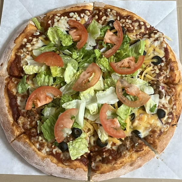 A Ruszoni's Pizza taco pizza topped with lettuce, tomatoes, black olives, and shredded cheese.