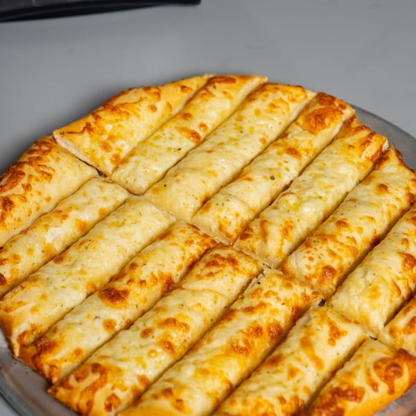 Close-up of Ruszoni's cheesy breadsticks, golden brown and covered in melted cheese, on a metal pizza pan.