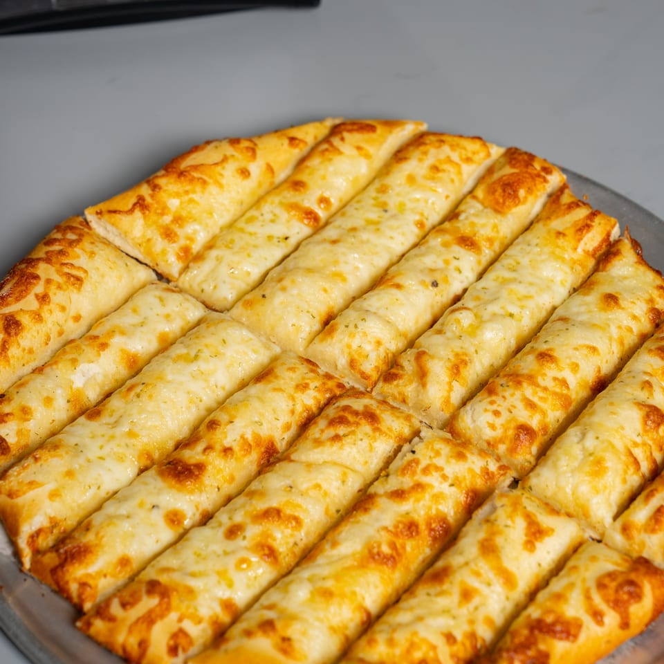 Close-up of Ruszoni's cheesy breadsticks, golden brown and covered in melted cheese, on a metal pizza pan.