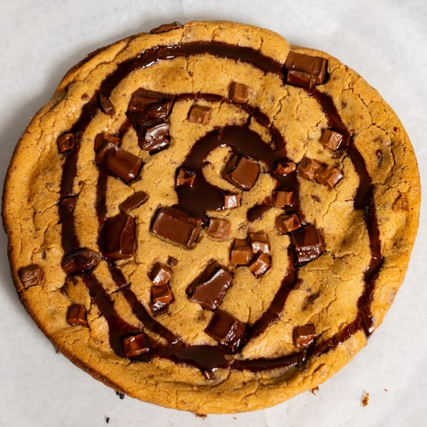 A large, round Ruszoni's Pizza chocolate chip cookie with melted chocolate chunks and drizzle.