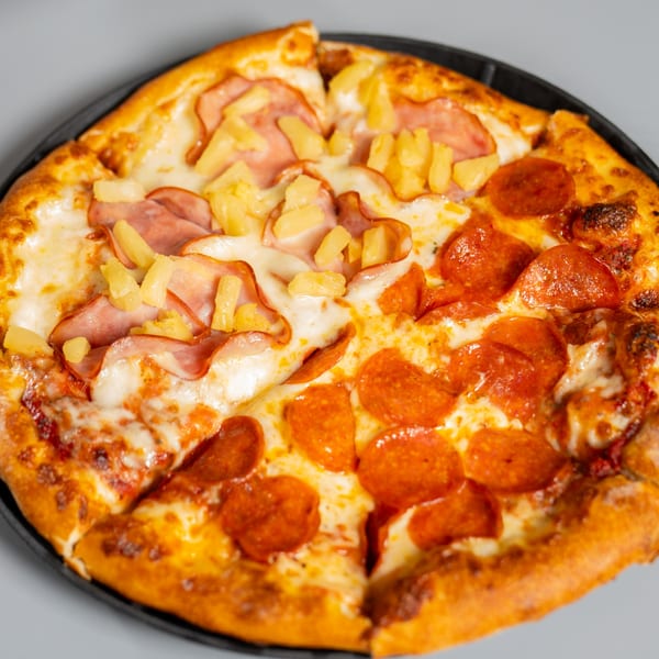 A Ruszoni's Pizza with half pepperoni and half ham and pineapple on a gray background.