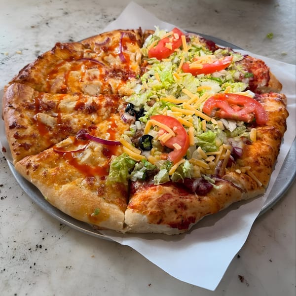 Ruszoni's Pizza with half BBQ chicken and half taco pizza, topped with fresh lettuce and tomatoes.