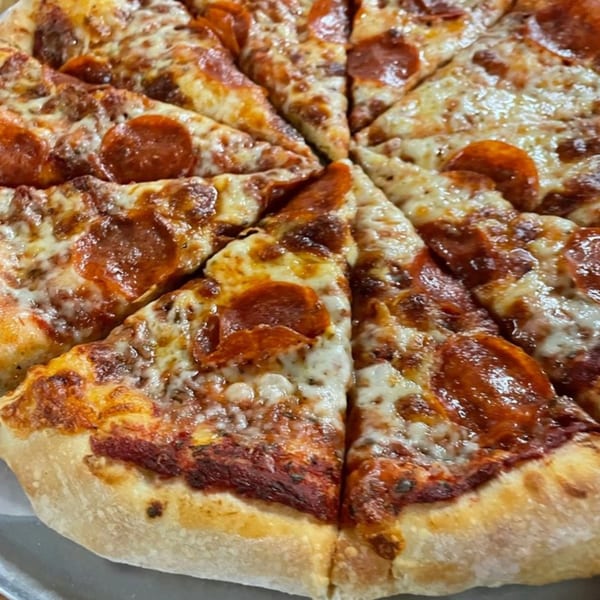 A close-up of a freshly baked Ruszoni's pepperoni pizza, cut into slices, with melted cheese and a golden crust.